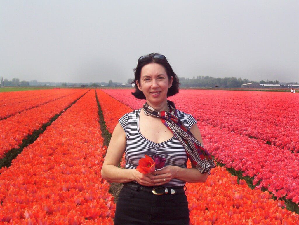 An image of Jean holding two tulips as she stands beside a field of orange tulips near Lisse in the Netherlands. Photography by Frame To Frame - Bob and Jean.