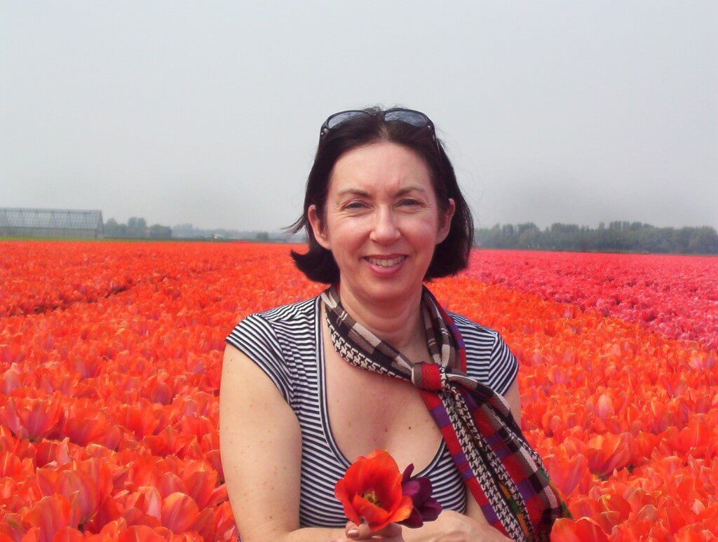 An image of Jean holding two tulips as she stands beside a field of orange tulips near Lisse in the Netherlands. Photography by Frame To Frame - Bob and Jean.