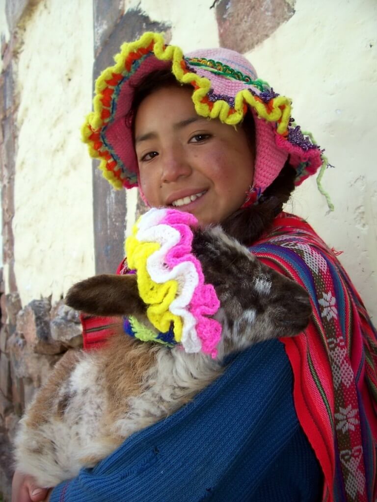 A little girl in traditional dress holds her goat on a Cusco street, peru