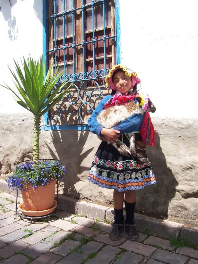 A little girl in traditional dress holds her goat on a Cusco street, peru