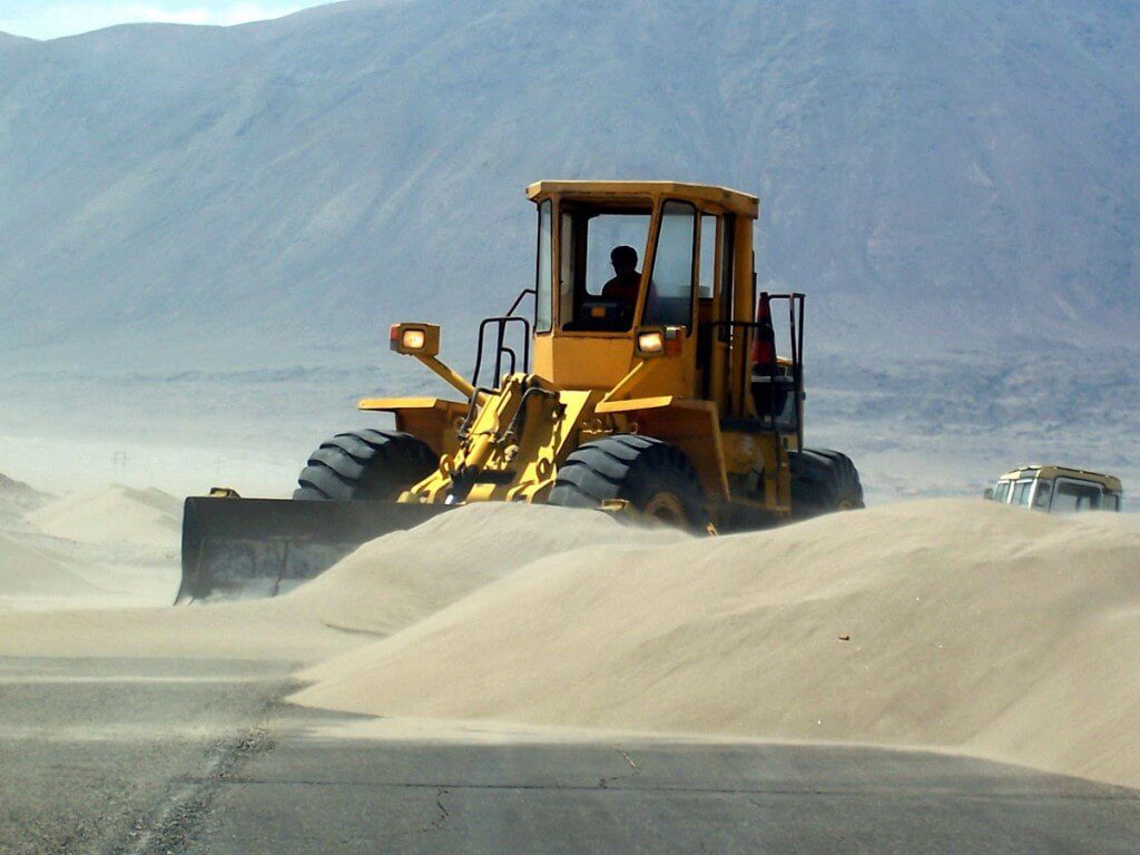 front end loader clears sand off pan american highway - peru