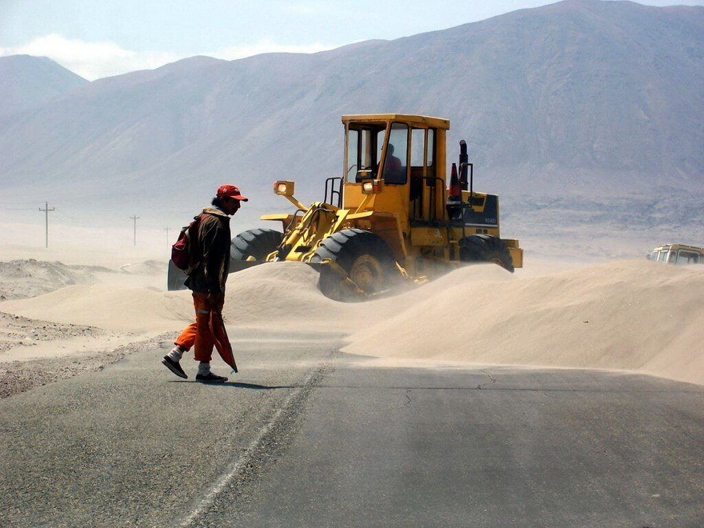 workers clear sand off pan american highway - peru