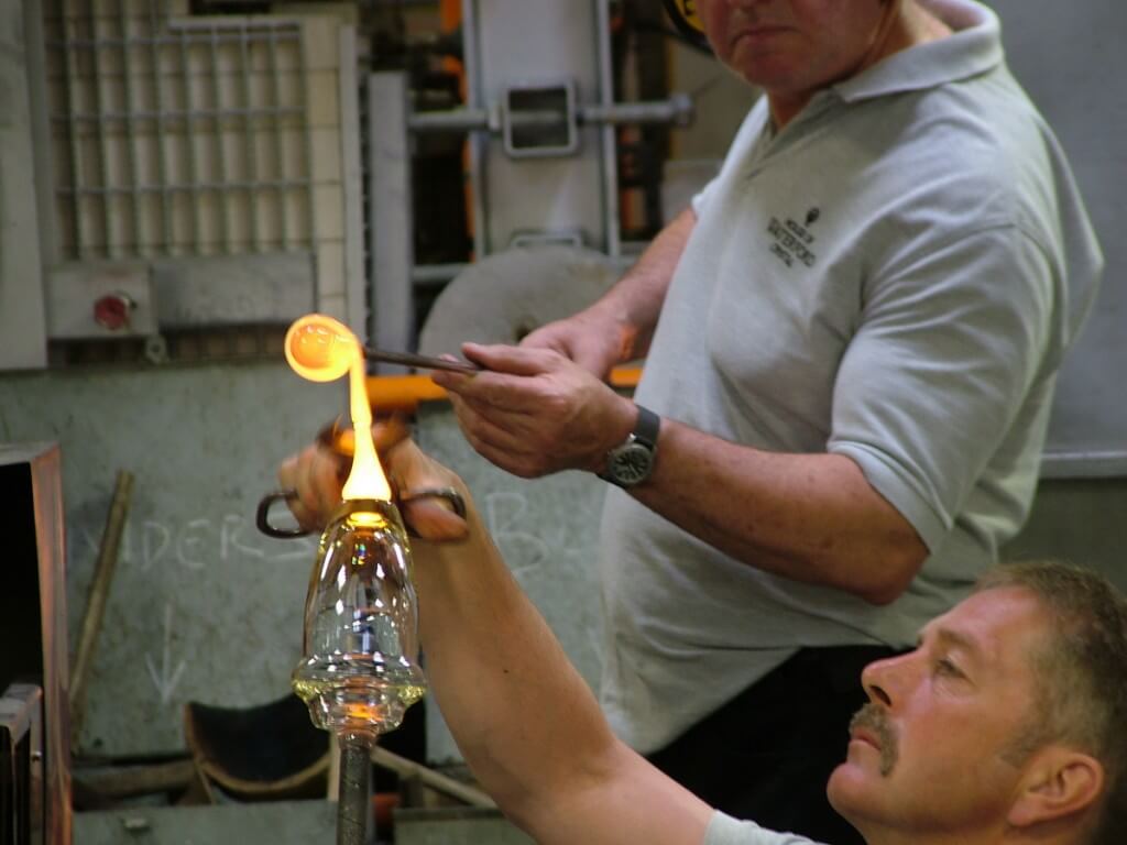 An image of glass blowers attaching molten glass to the base of crystal vase at the Waterford Crystal factory in Waterford, Ireland. Photography by Frame To Frame - Bob and Jean.