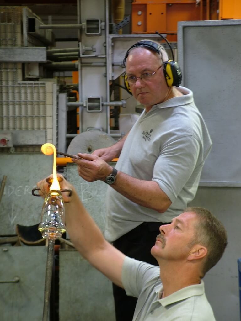 An image of glass blowers attaching molten glass to the base of crystal vase at the Waterford Crystal factory in Waterford, Ireland. Photography by Frame To Frame - Bob and Jean.