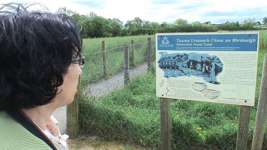 An image of Jean reading the information sign at the Brownshill Portal Tomb in County Carlow, Ireland. Photography by Frame To Frame - Bob and Jean.