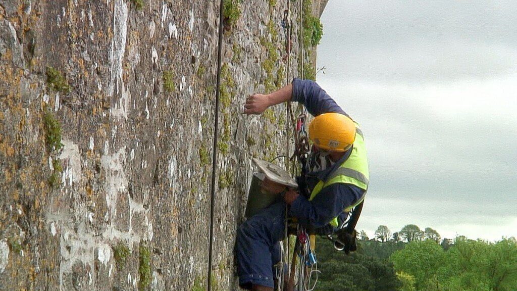 stone mason adds mortar to outer wall of blarney castle, ireland