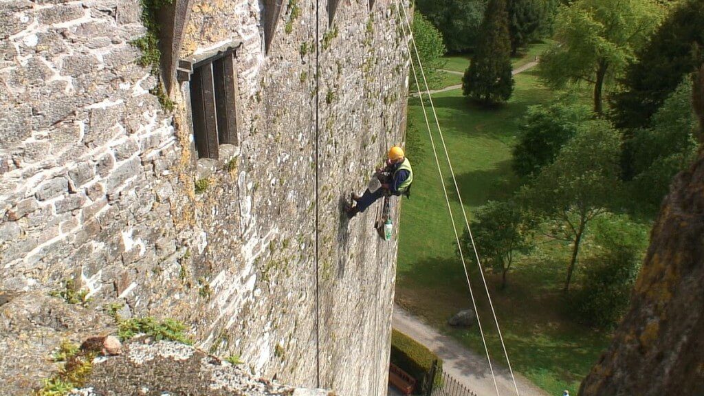 stone mason repairs outer wall of blarney castle, county cork, ireland