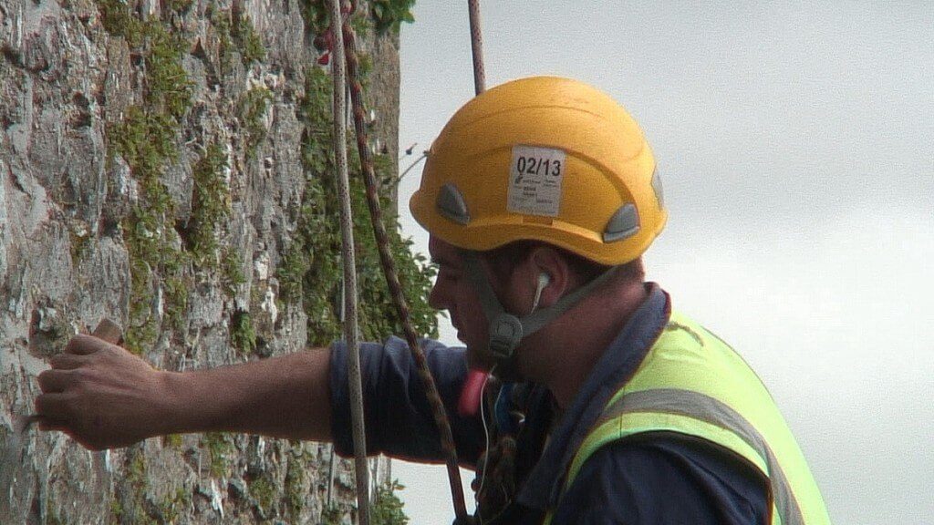 stone mason repairs outer wall of blarney castle, ireland