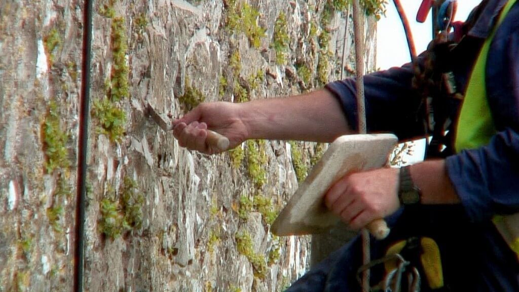 stone mason repairs wall of blarney castle with new mortar, ireland