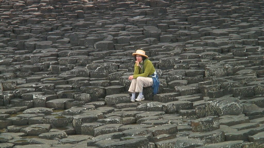 An image of Jean sitting among the hexagonal basalt columns at the Giant's Causeway, near Portrush, Northern Ireland. Photography by Frame To Frame - Bob and Jean.