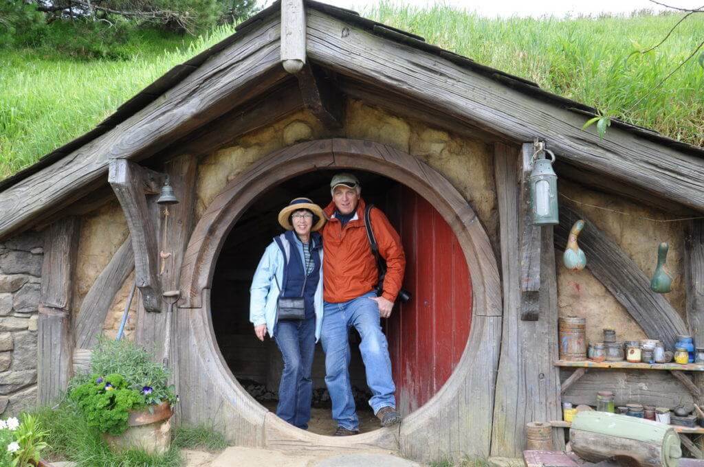An image of Bob and Jean standing in the doorway of the gourd artists hobbit hole at Hobbiton in New Zealand. Photography by Frame To Frame - Bob and Jean.