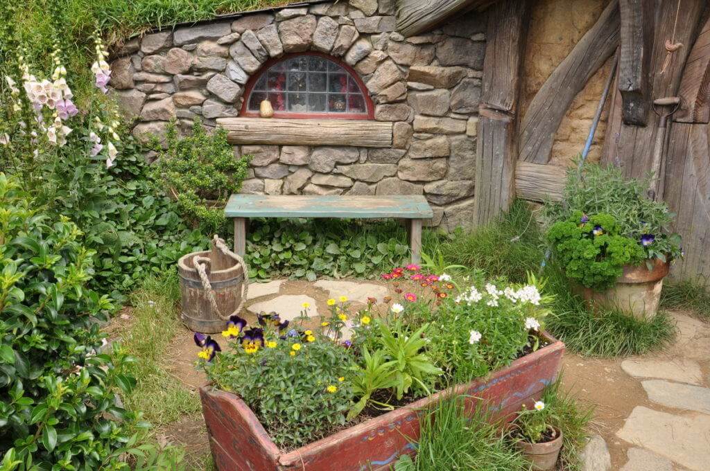 An image of the flower gardens and a stone window in the Gourd Artists home at Hobbiton in New Zealand. Photography by Frame To Frame - Bob and Jean.