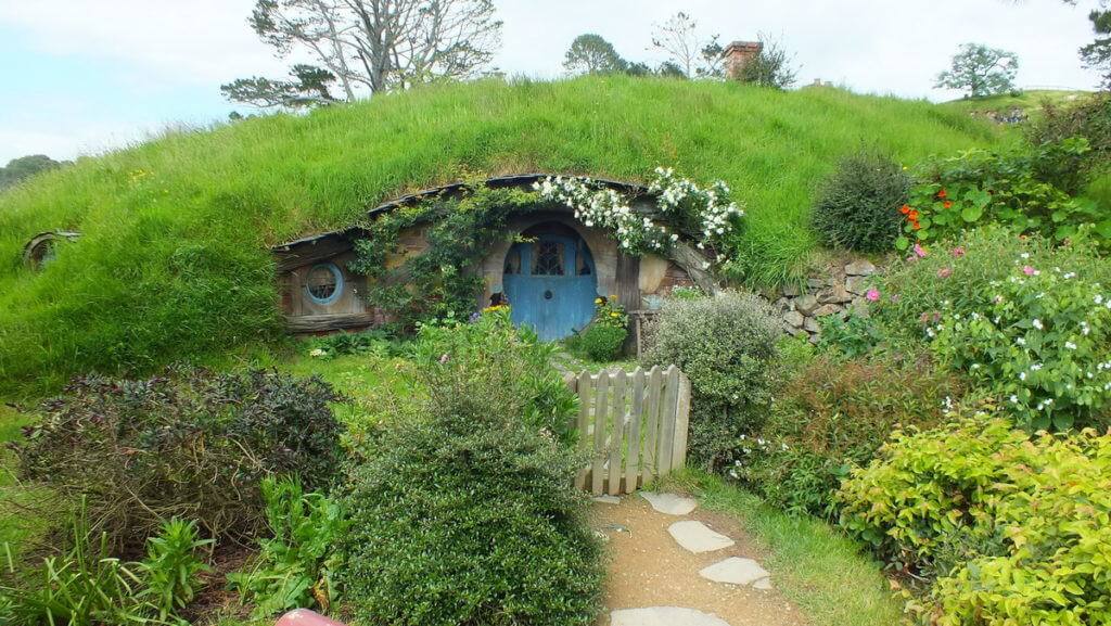 An image of a hobbit hole with a blue door in the side of a hill at Hobbiton in New Zealand. Photography by Frame To Frame - Bob and Jean.