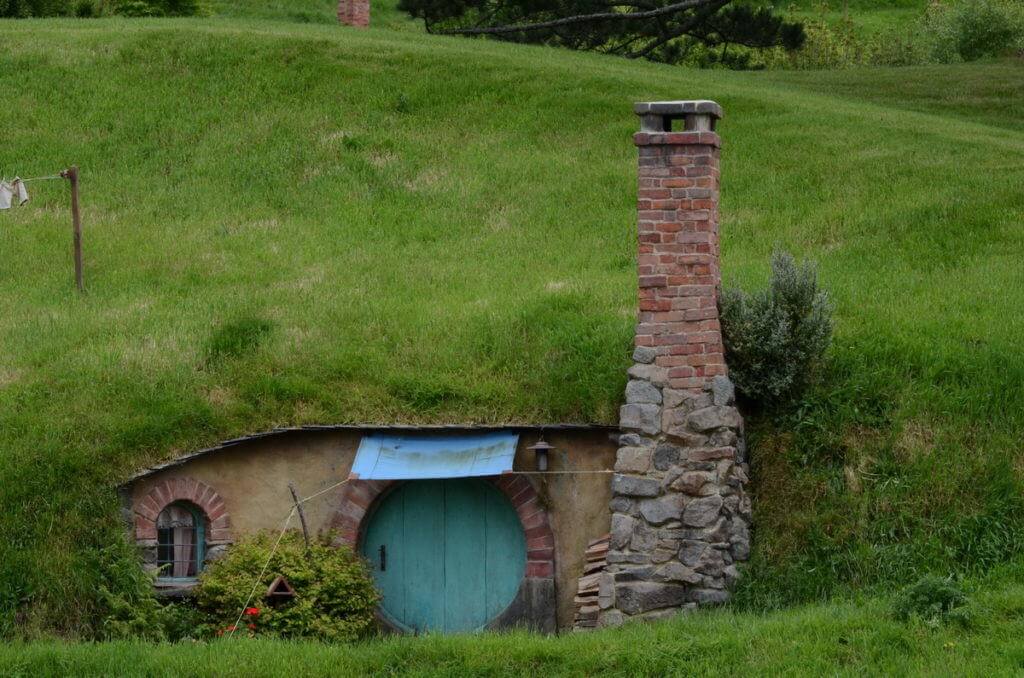 An image of a hobbit hole with a blue door and a tall chimney at Hobbiton in New Zealand. Photography by Frame To Frame - Bob and Jean.