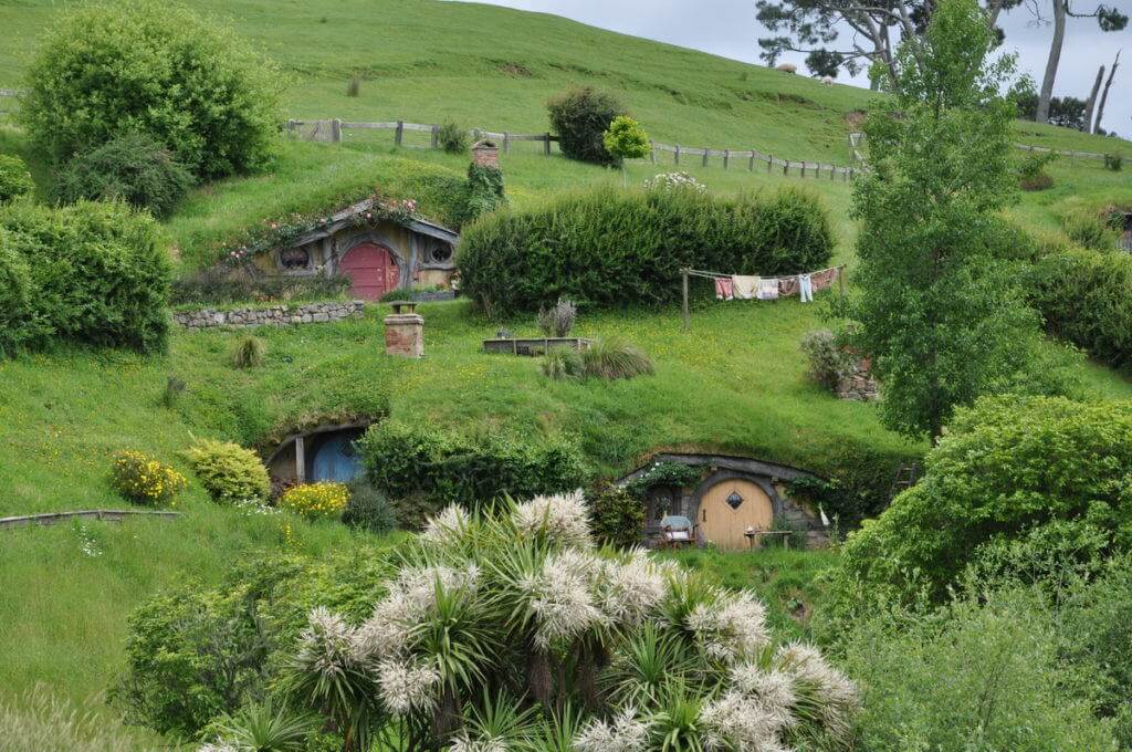 An image of various hobbit holes on the side of a green hills at Hobbiton in New Zealand. Photography by Frame To Frame - Bob and Jean.