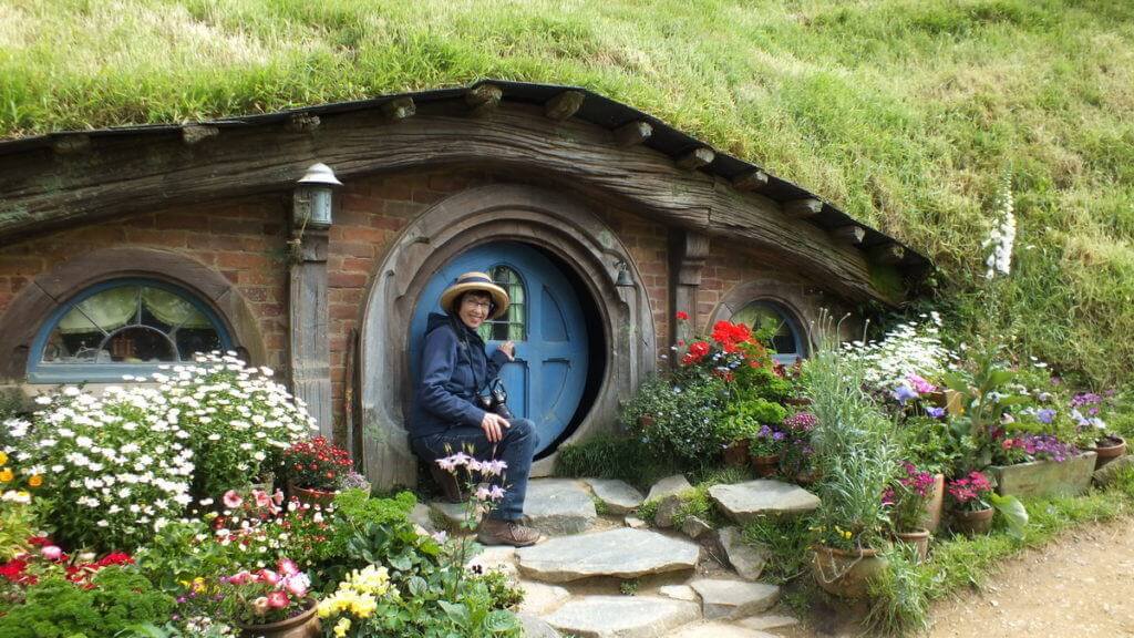 An image of a Jean opens a hobbit hole door at Hobbiton in New Zealand. Photography by Frame To Frame - Bob and Jean.