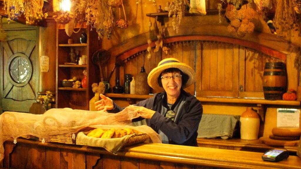 An image of Jean offering cookies for sale behind the main counter at the Green Dragon Pub at Hobbiton in New Zealand. Photography by Frame To Frame - Bob and Jean.