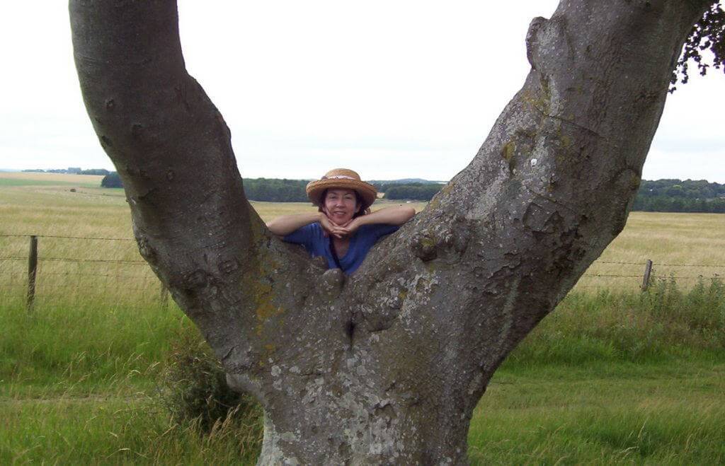 An image of Jean standing beside a Y shaped tree near Stonehenge in Wiltshire, England. Photography by Frame To Frame - Bob and Jean