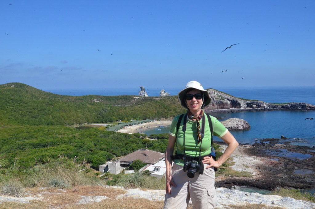 An image of Jean standing on the Isla Isabel with the fishing harbour behind her in Mexico. Photography by Frame To Frame - Bob and Jean.