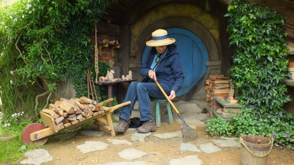 An image of a Jean using a hobbit leaf rake at Hobbiton in New Zealand. Photography by Frame To Frame - Bob and Jean.