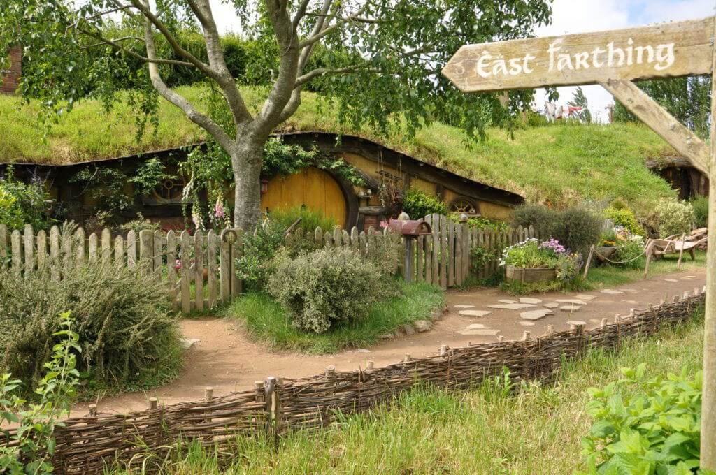 An image of the East Farthing street sign in front of Sams House with a yellow door and beautiful gardens at Hobbiton in New Zealand. Photography by Frame To Frame - Bob and Jean.