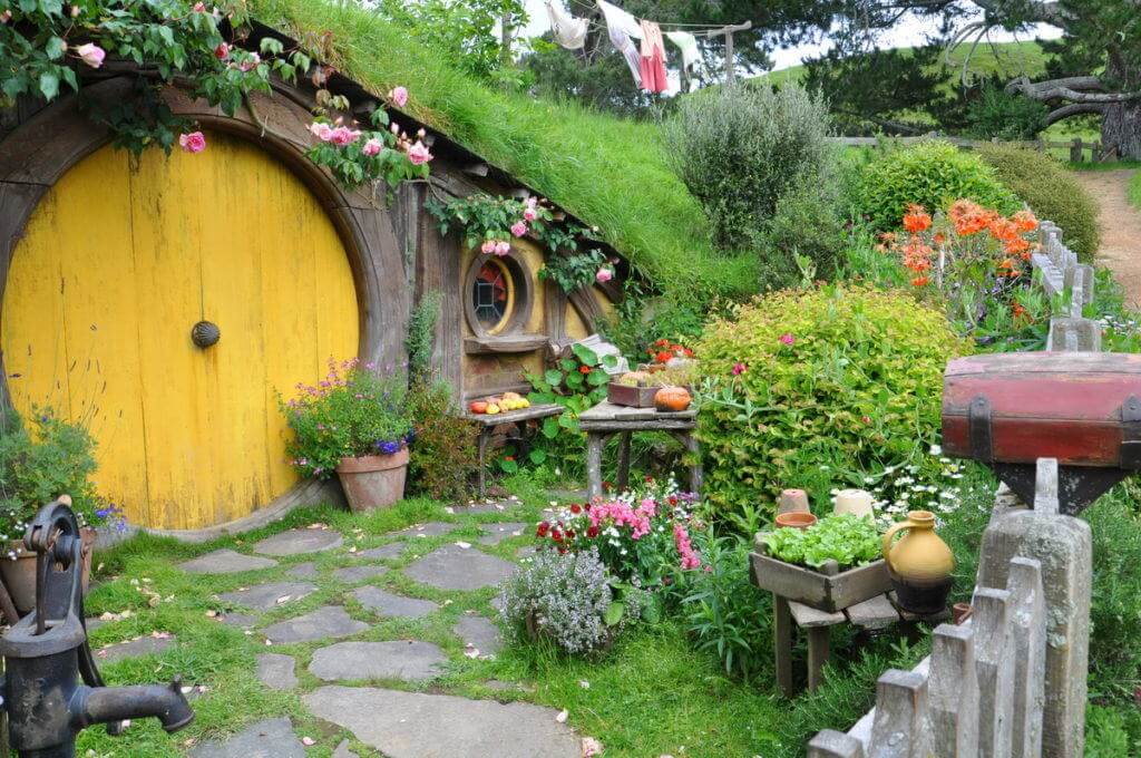 An image of Sams House with a yellow door and beautiful gardens at Hobbiton in New Zealand. Photography by Frame To Frame - Bob and Jean.