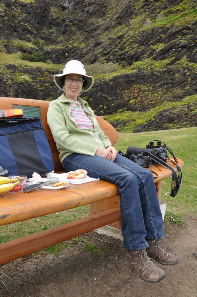 An image of Jean sitting on a park bench at Muriwai Regional Park in New Zealand.