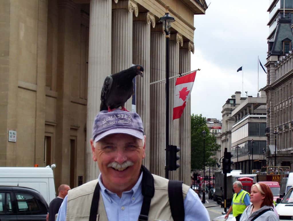 An image of pigeon sitting on a person's head in Trafalgar Square in London, England.