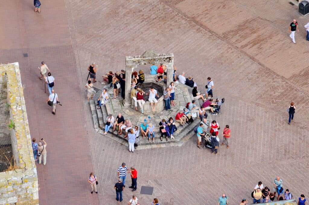 Image of tourists sitting at the drinking well in Piazza della Cisterna in San Gimignano, Italy.