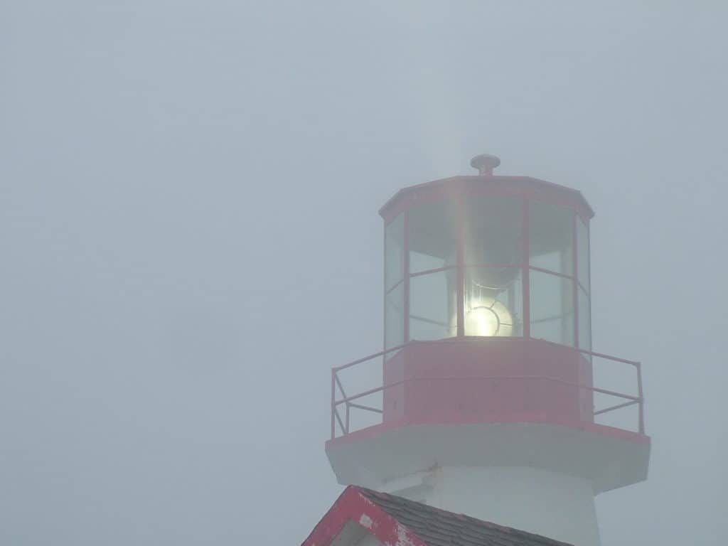 lighthouse beaming light through fog, quirpon island, newfoundland, canada