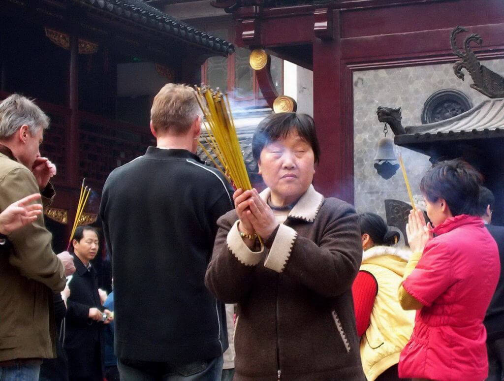 A woman prays to the gods will holding incense sticks inside the City God Temple of Shanghai.