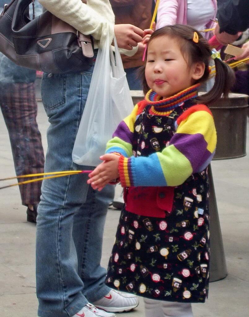A young girl prays will holding her incense sticks outside the City God Temple of Shanghai.