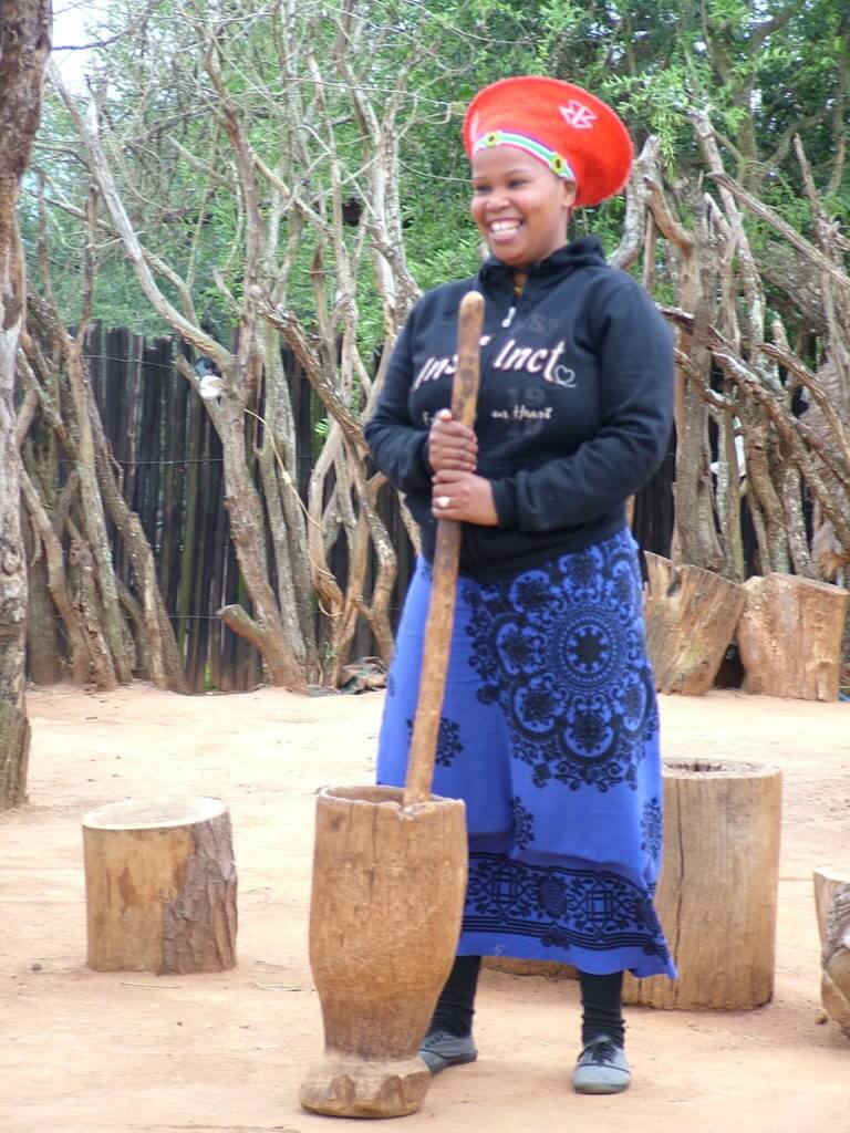 a married zulu woman grinding sorghum, shakaland, kwazulu-natal, south africa