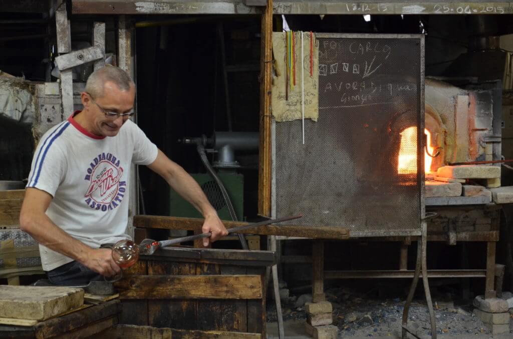 an artisan at his workbench with giant glass-cutting clippers, gino mazzuccato glass factory, murano island, venice, italy