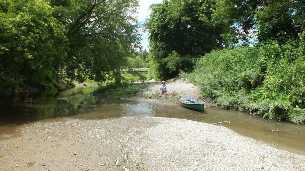 Image of Jean sitting beside our canoe along Duffins Creek in Ajax, Ontario, Canada.