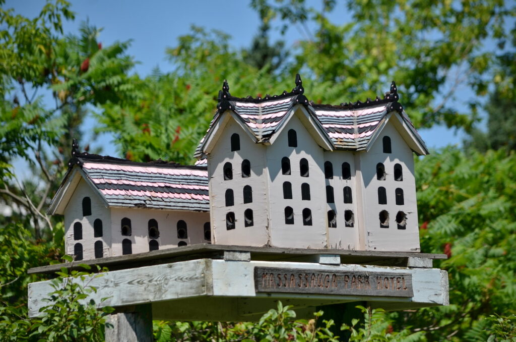 image of massassauga park hotel birdhouse, The late Doug Harns, a former superintendent with the PE Region Conservation had a gift working with wood and it was through his creativity that birdhouse city was born. Starting with a massive birdhouse replica of the historic Massassauga Park Hotel (which used to stand on the grounds of Massassauga Point Conservation Area before being demolished in the 1940s), the city was created when it was decided that if one birdhouse looked good, then a few more would look better.