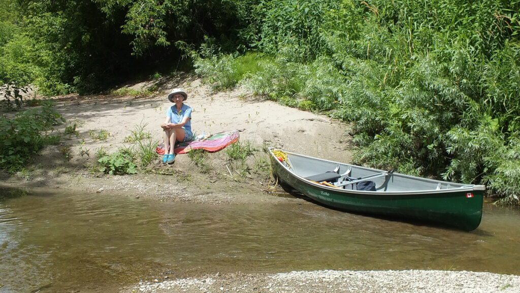 Image of Jean sitting beside our canoe along Duffins Creek in Ajax, Ontario, Canada.