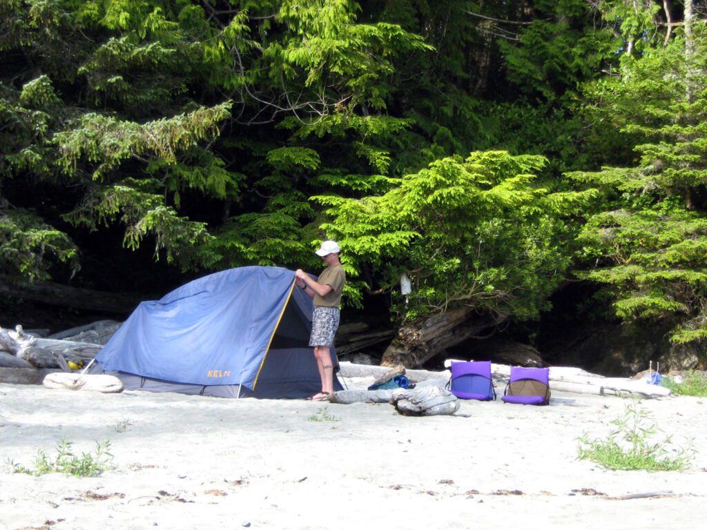 image of person pitching a tent on a sandy beach, ahous bay, vargas island, british columbia 