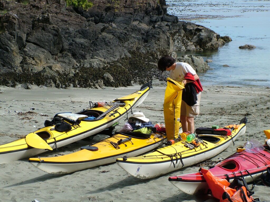 image of people and kayaks on a sandy beach, ahous bay, vargas island, british columbia 
