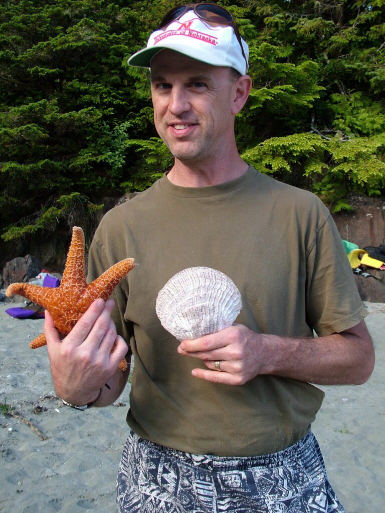 image of a man holding a starfish and shell, ahous bay, vargas island, british columbia